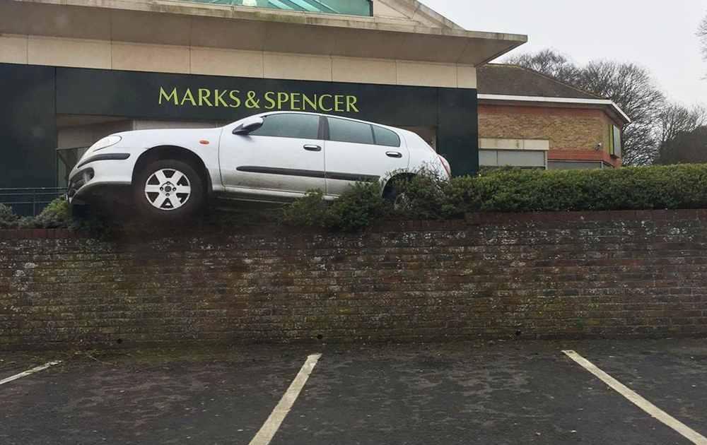 CAR MOUNTS WALL AT ENTRANCE TO MORRISONS