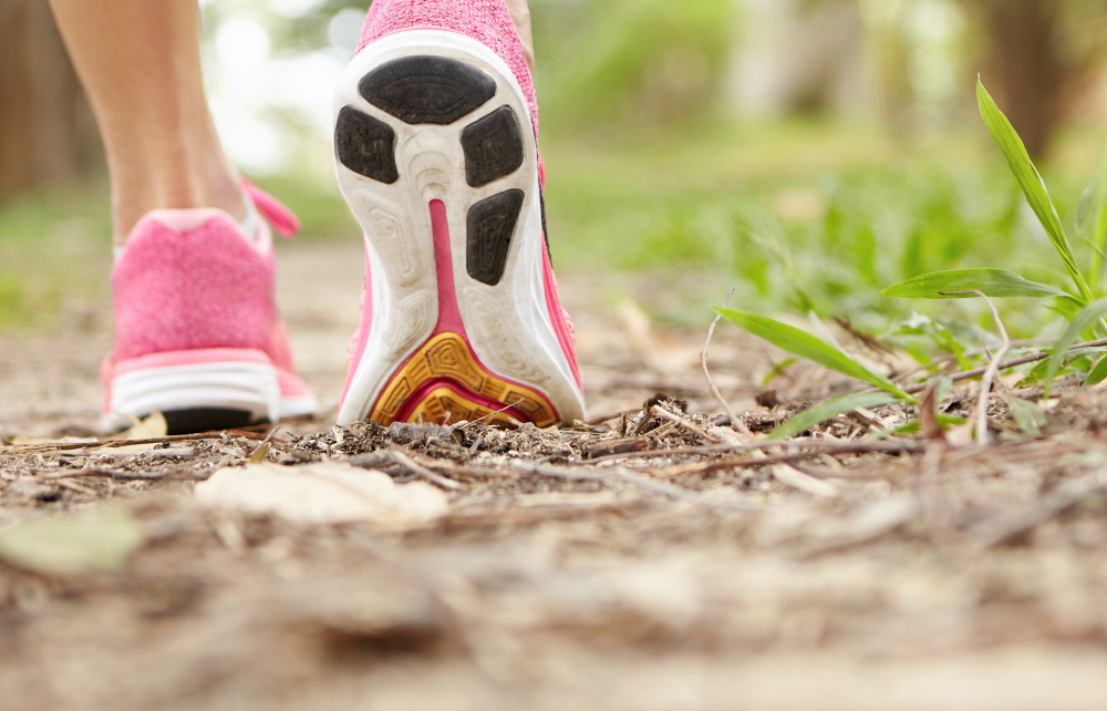Cropped Shot Of Athlete Girl In Pink Running Shoes Hiking In Forest On Sunny Day. Fit Slim Legs Of Sporty Female In Sneakers During Jogging Workout. Selective Focus On Sole. Shallow Depth Of Field