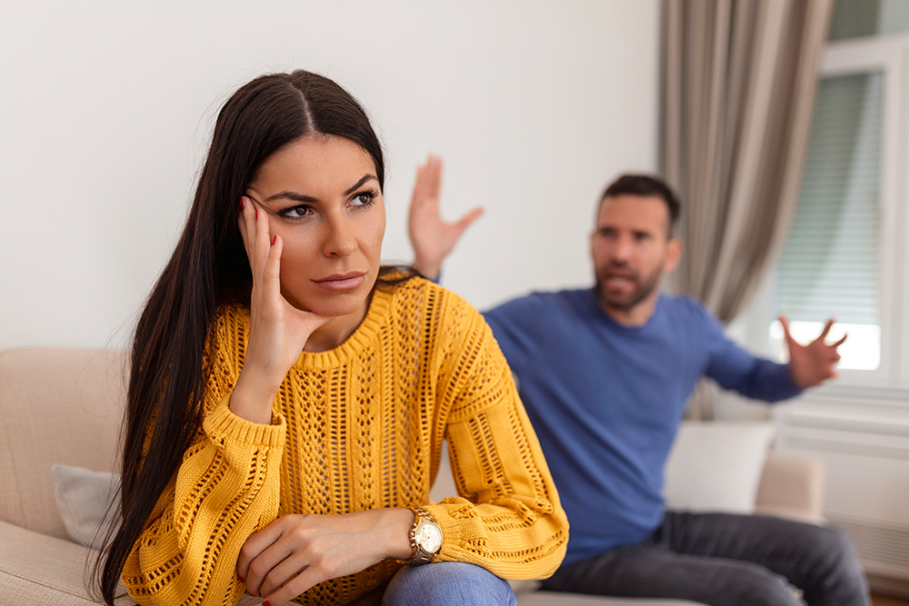 Young Couple Having Argument - Conflict, Bad Relationships. Angry Fury Woman. Angry Young Couple Sit On Couch In Living Room Having Family Fight Or Quarrel Suffer From Misunderstanding