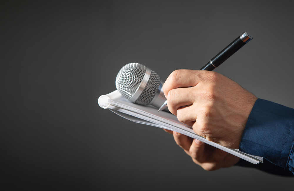 Caucasian Journalist Holding Microphone, Notepad And Pen.