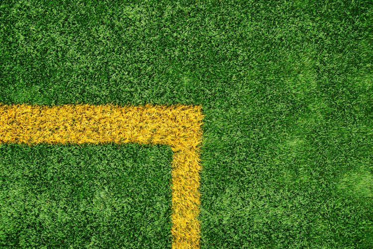 Top-down view of a bright yellow corner line painted on a lush green artificial turf football pitch.